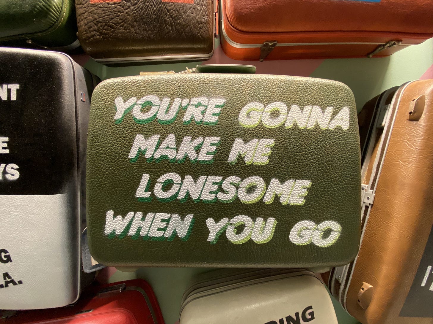 A vintage suitcase (tucked in a pile) reads, “You’re gonna make me lonesome when you go.”
