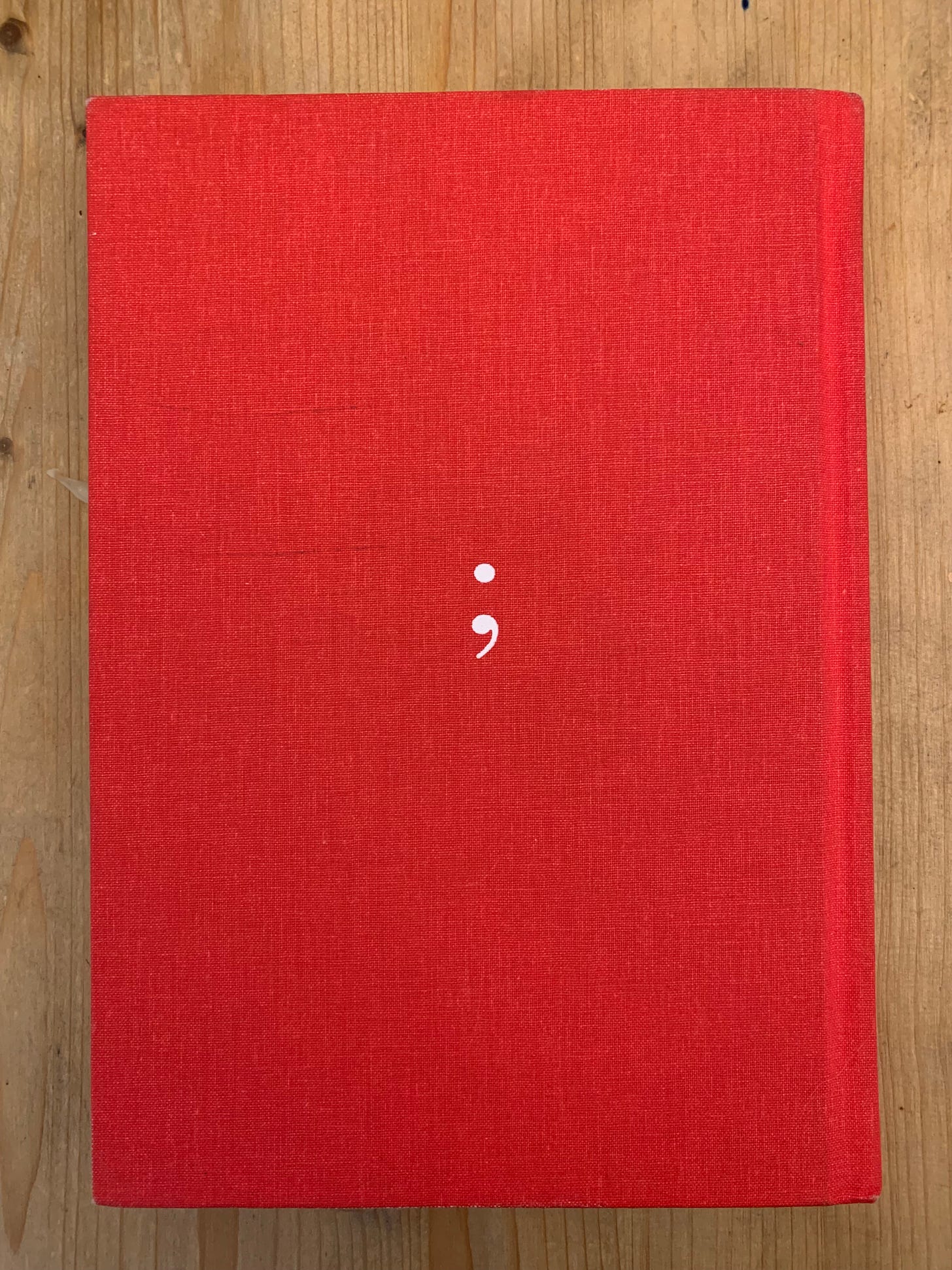 Picture of the back of the Elements of Style, featuring a white semi colon on a red background. 