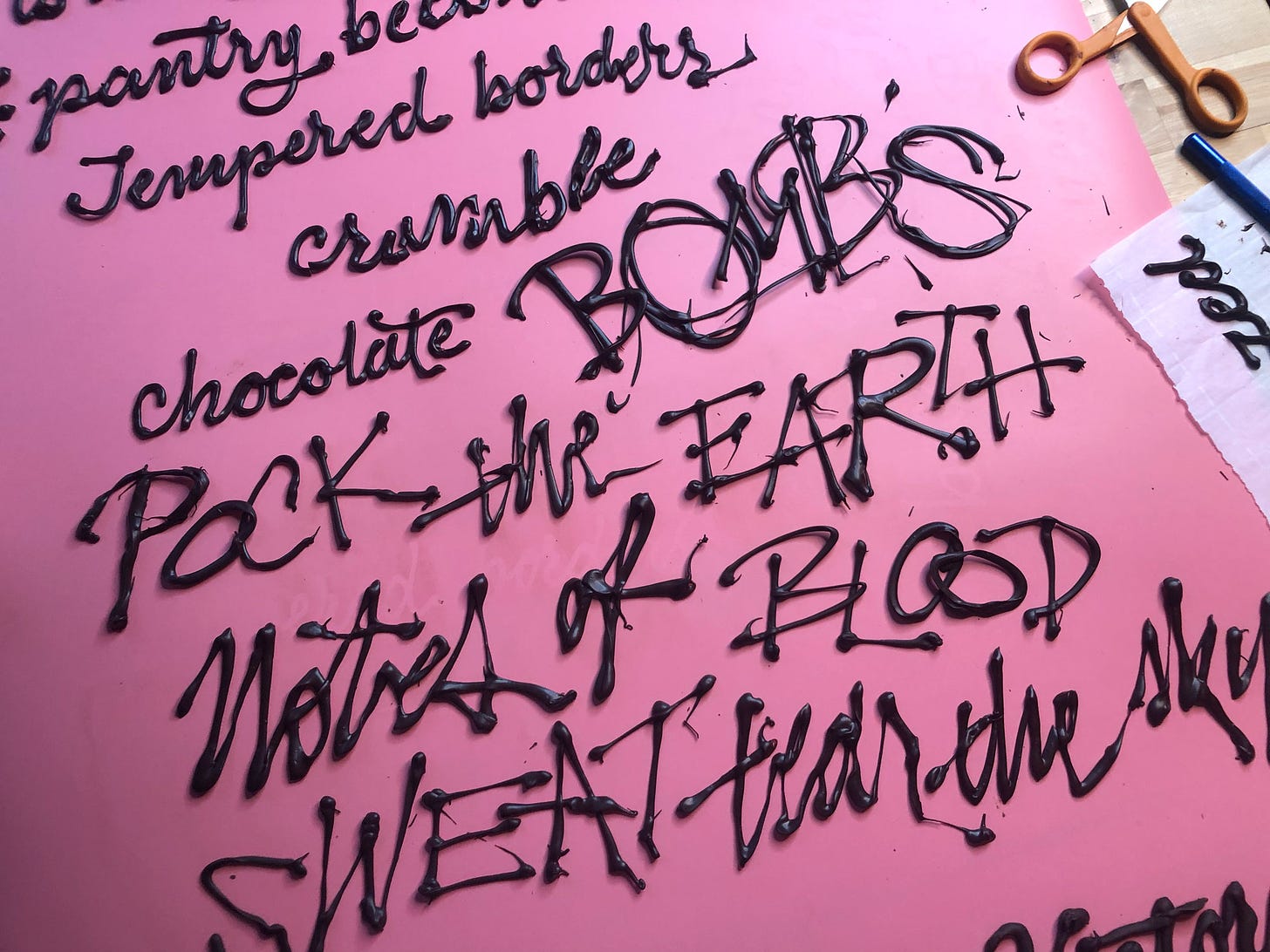 Chocolate words are piped onto a smooth background. In the top right corner is parchment paper with leftover letters and a pair of scissors. It says "tempered borders crumble / chocolate BOMBS / POCK the EARTH / Notes of BLOOD / SWEAT / tear the sky"