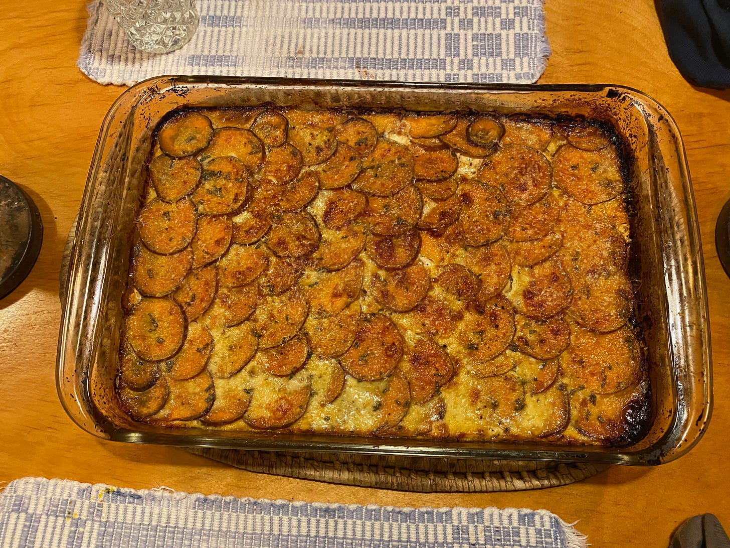 A sweet potato casserole, golden brown and bubbling, in a glass baking dish on a dinning room table.