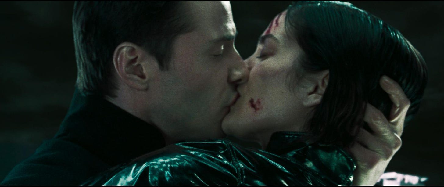 Film still from The Matrix. Neo and Trinity are in a passionate kiss. Trinity has cuts and blood on her face.