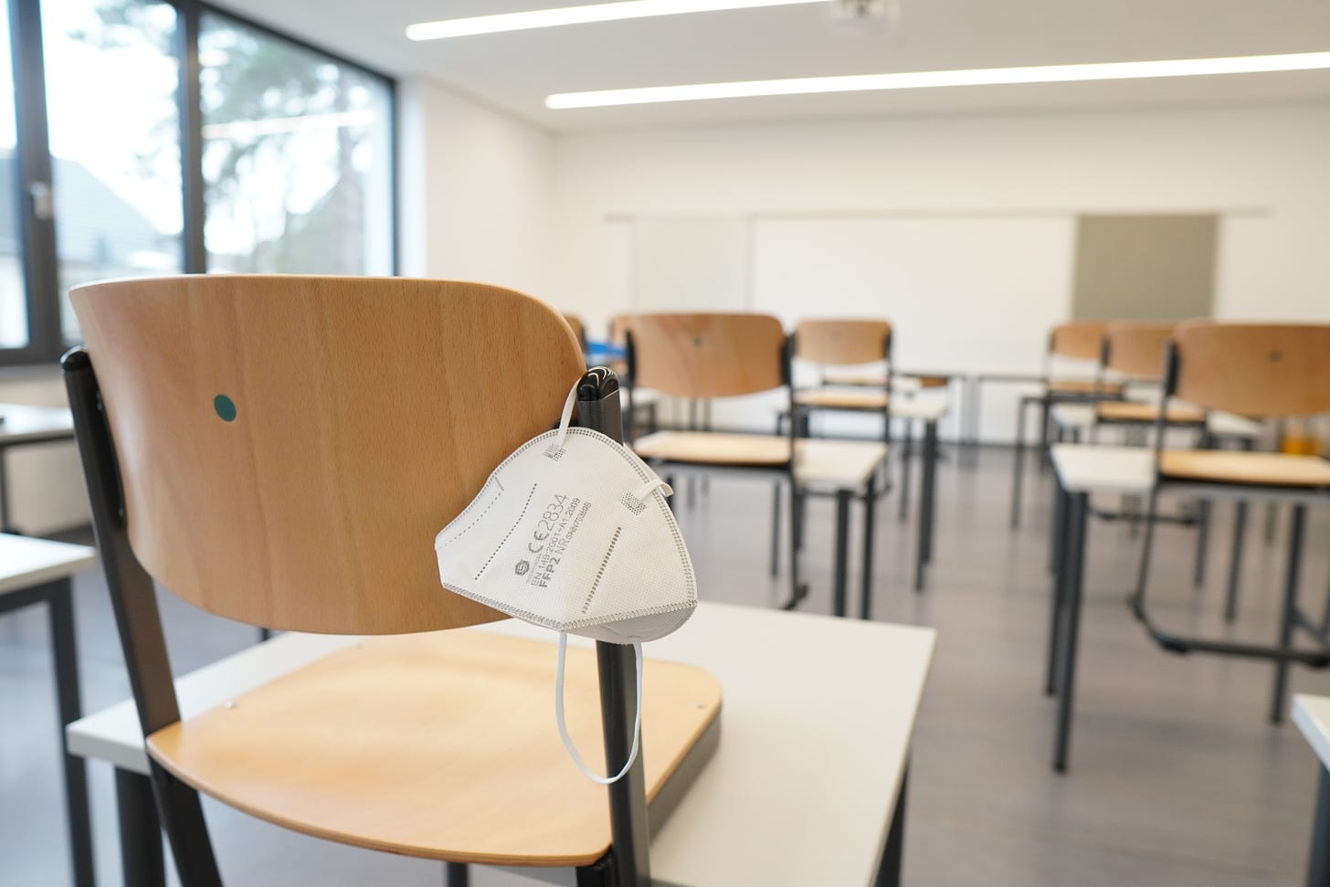 a white surgical mask hangs from an empty school chair in an empty classroom