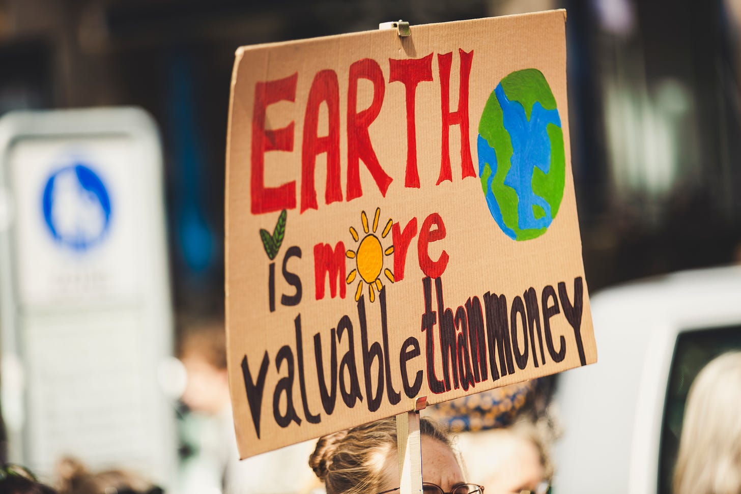 A cardboard protest sign reads "Earth is more valuable than money."