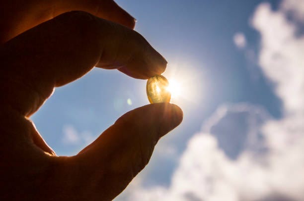 la vitamina d mantiene sano mientras que la falta de sol. cápsula de cáscara suave amarillo vitamina d contra el cielo azul y sol en día soleado. concepto de curación. - vitamina d fotografías e imágenes de stock