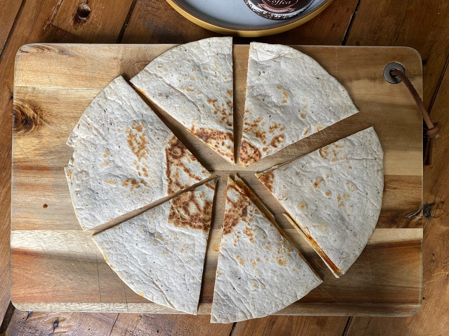 Wooden chopping board topped with a toasted tortilla wrap cut into six pieces.
