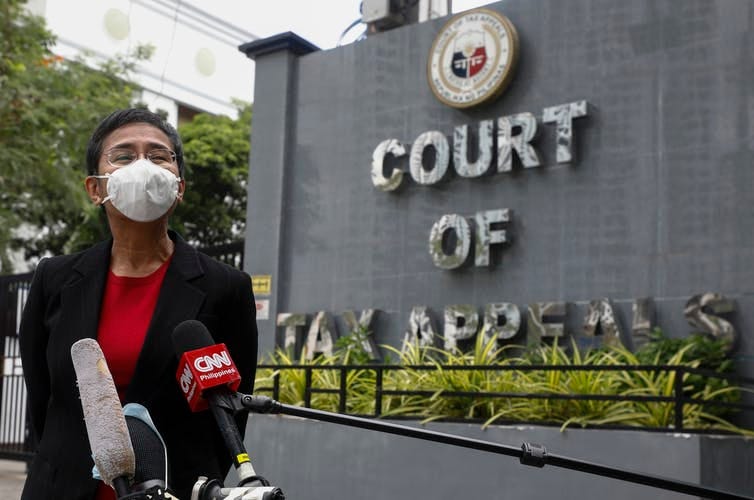 Maria Ressa wearing a face mask, speaking into microphones, next to Court of Tax Appeals sign.