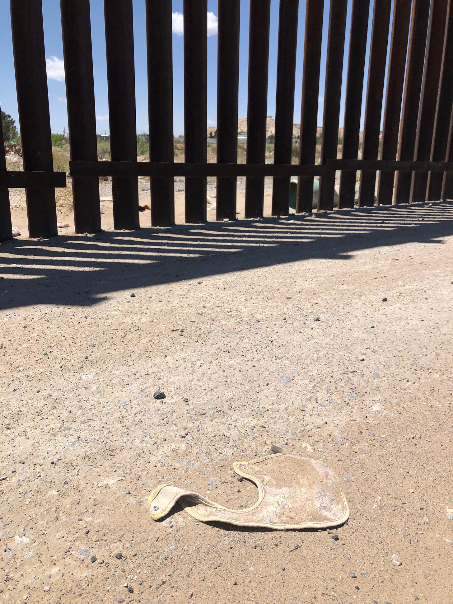 Photo of a dirty, discarded baby bib with the border wall visible in the background.