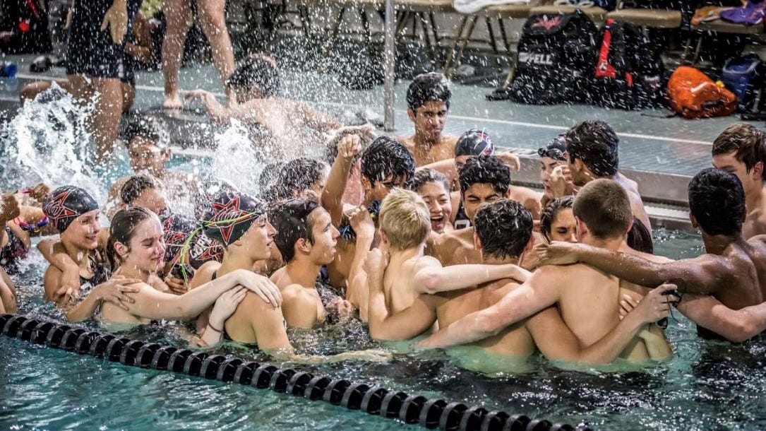 Two dozen high school swimmers celebrating in a single lane of a pool