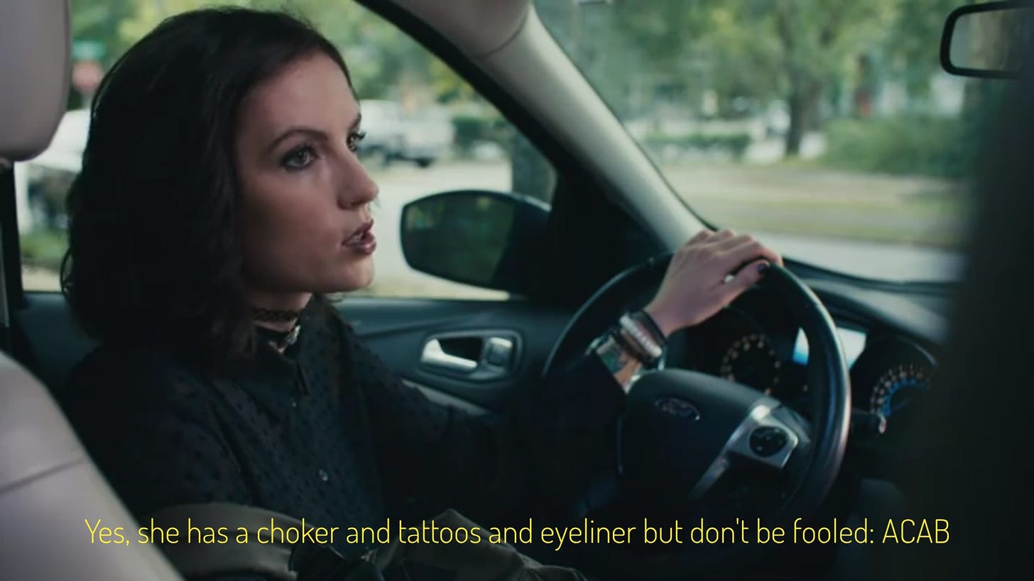 Val in her car, captioned "Yes, she has a choker and tattoos and eyeliner but don't be fooled: ACAB"