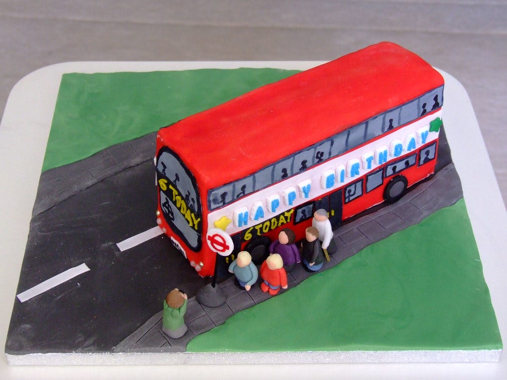 A bus birthday cake, showing people getting on the bus. It is a red double decker, which says happy birthday along the side