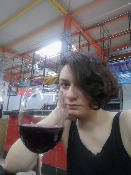 A bored looking woman in a market with a glass of wine