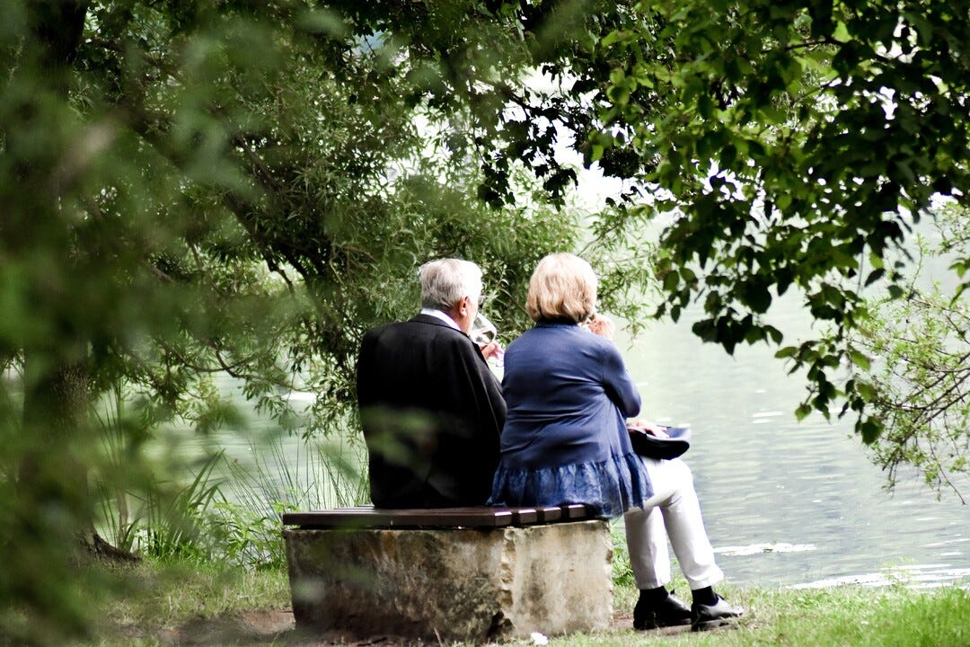 Photo by Sven Mieke via unsplash. Older couple sitting on a bench overlooking water