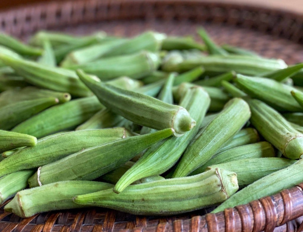 Fresh okra pods are spread on a brown basket.