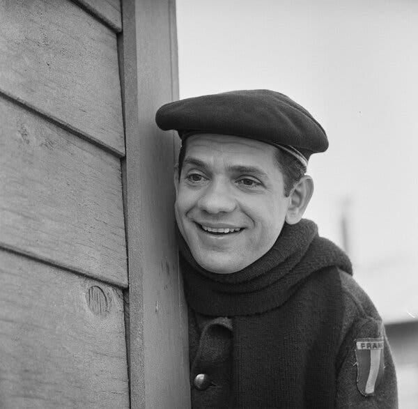 A black-and-white photo of Mr. Clary, wearing a beret and scarf, leaning against a wall.