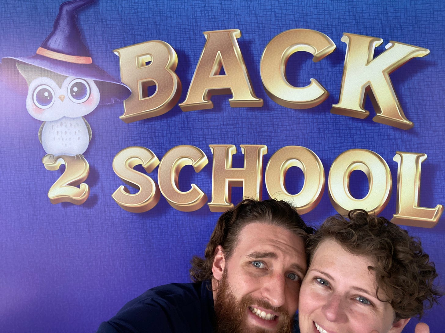 two people smiling at camera in front of a banner that says back to school