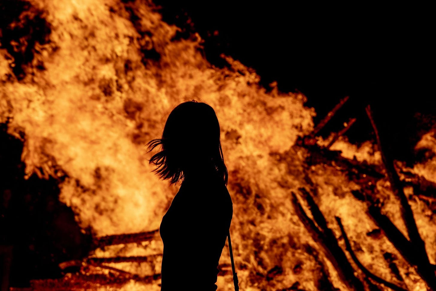 Image of fire burning with long-haired person profiled from behind, seeing just their outline