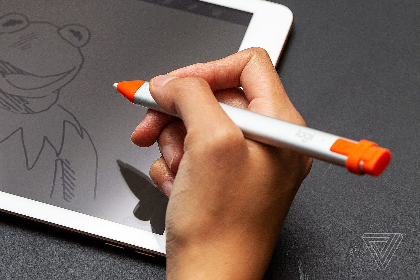 A photo of a hand holding a digital stylus over an iPad showing an illustration of Kermit the Frog.