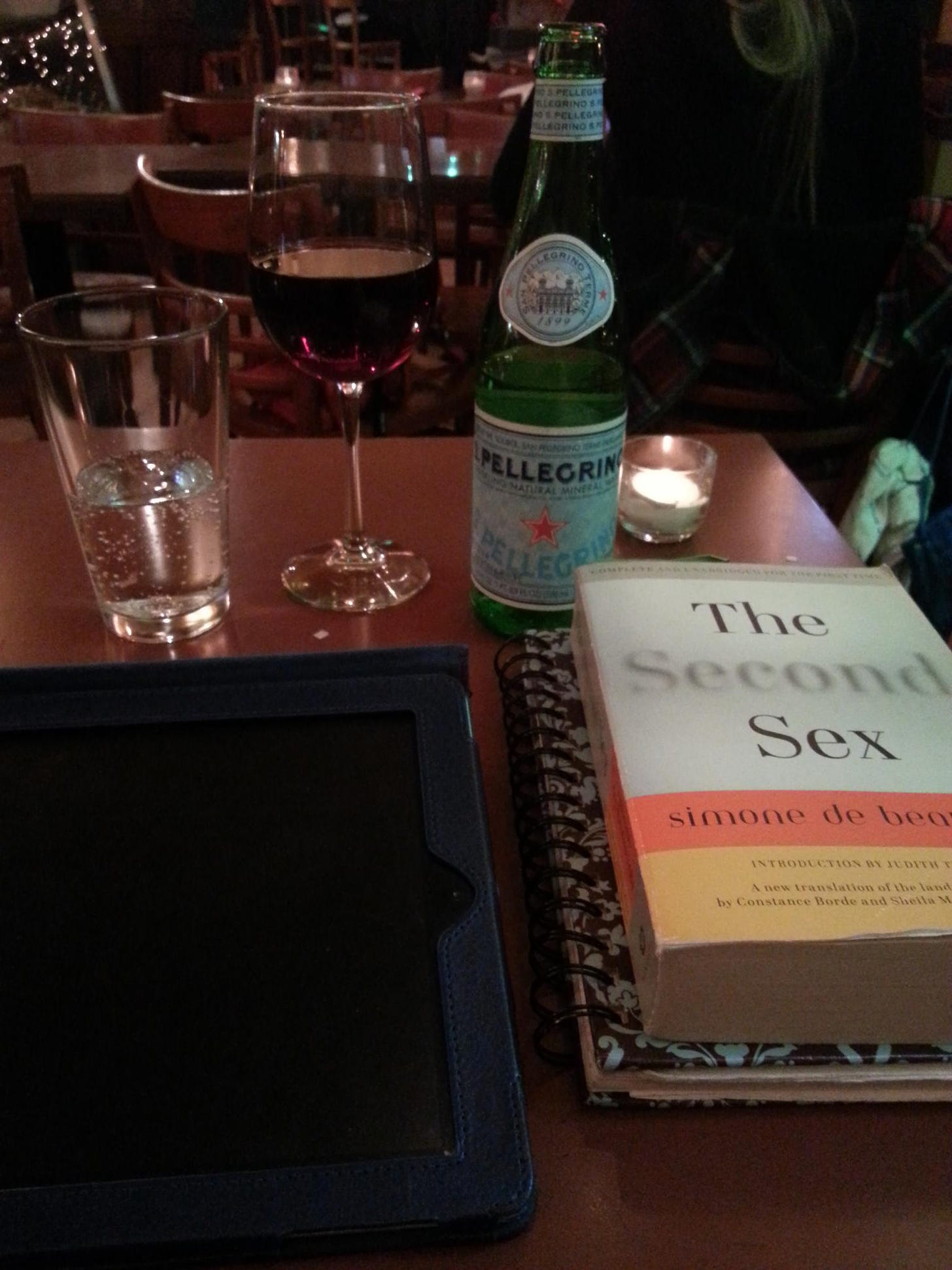 a table in a caffe with glasses of water and wine, a san pellegrino bottle, and a copy of 'the second sex' by simone de beauvoir