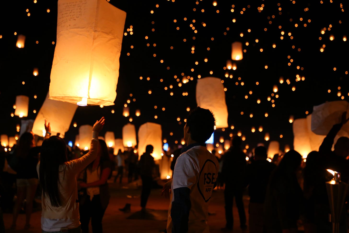 A crowd of people releasing kite lanterns into the night sky.