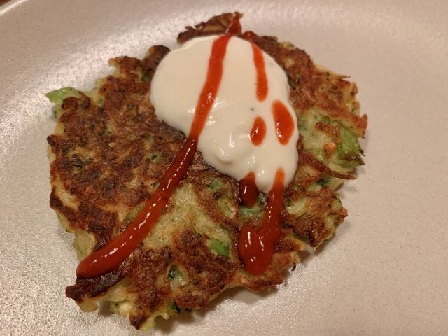 A browned broccoli fritter with a dollop of yogurt and a zigzag of sriracha on top