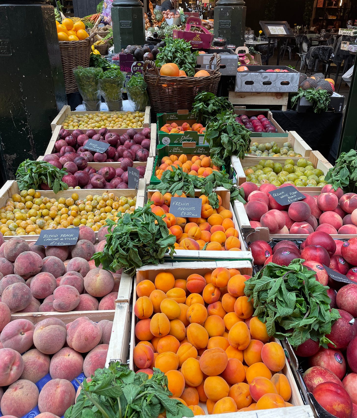 Photo of an indoor market stall with a colourful display of peaches, plums apricots, gooseberries and mint