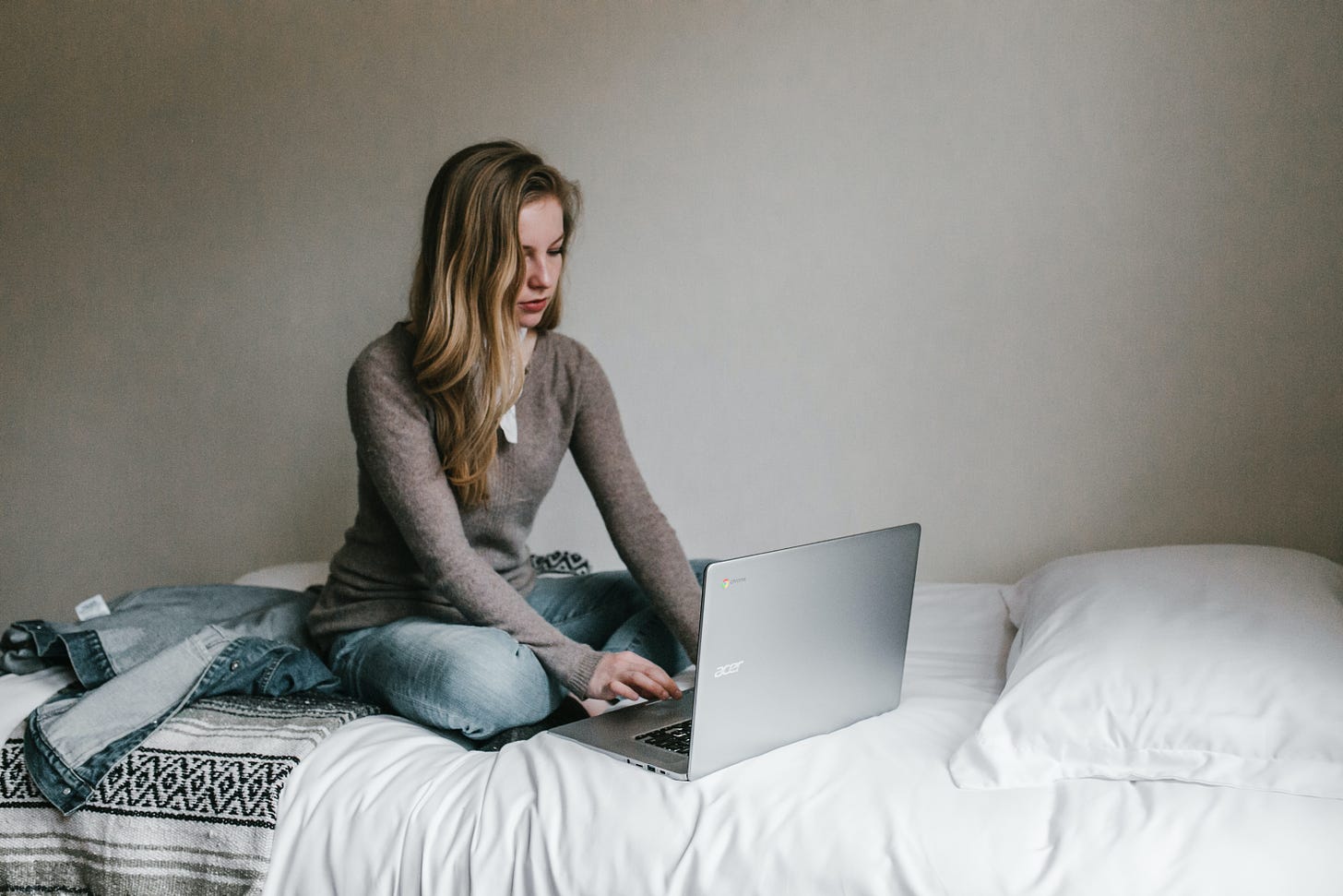 A woman types at a laptop sitting on a bed