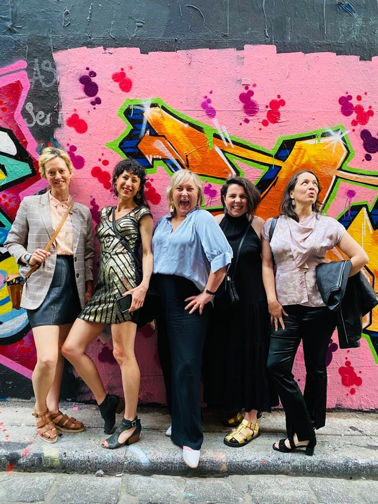 five women pose in front of bright street art