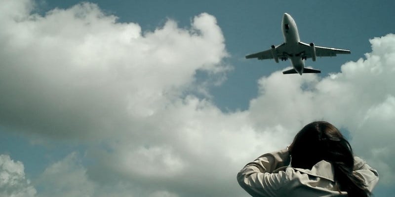 An aircraft takes off. In the foreground is a person with their hands over their ears