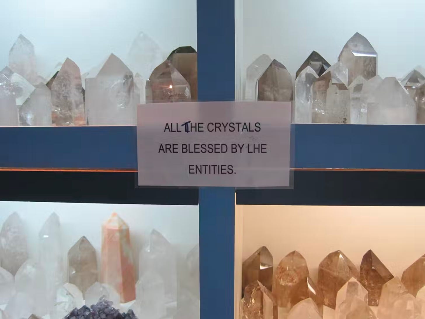 four different kinds of crystals behind a displace case, with a sign that says "All the crystals are blessed by LHE entities"