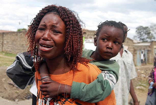 Woman cries while carrying a child on her back as they and others flee violence in their neighborhood during ethnic clashes in the central Kenyan...