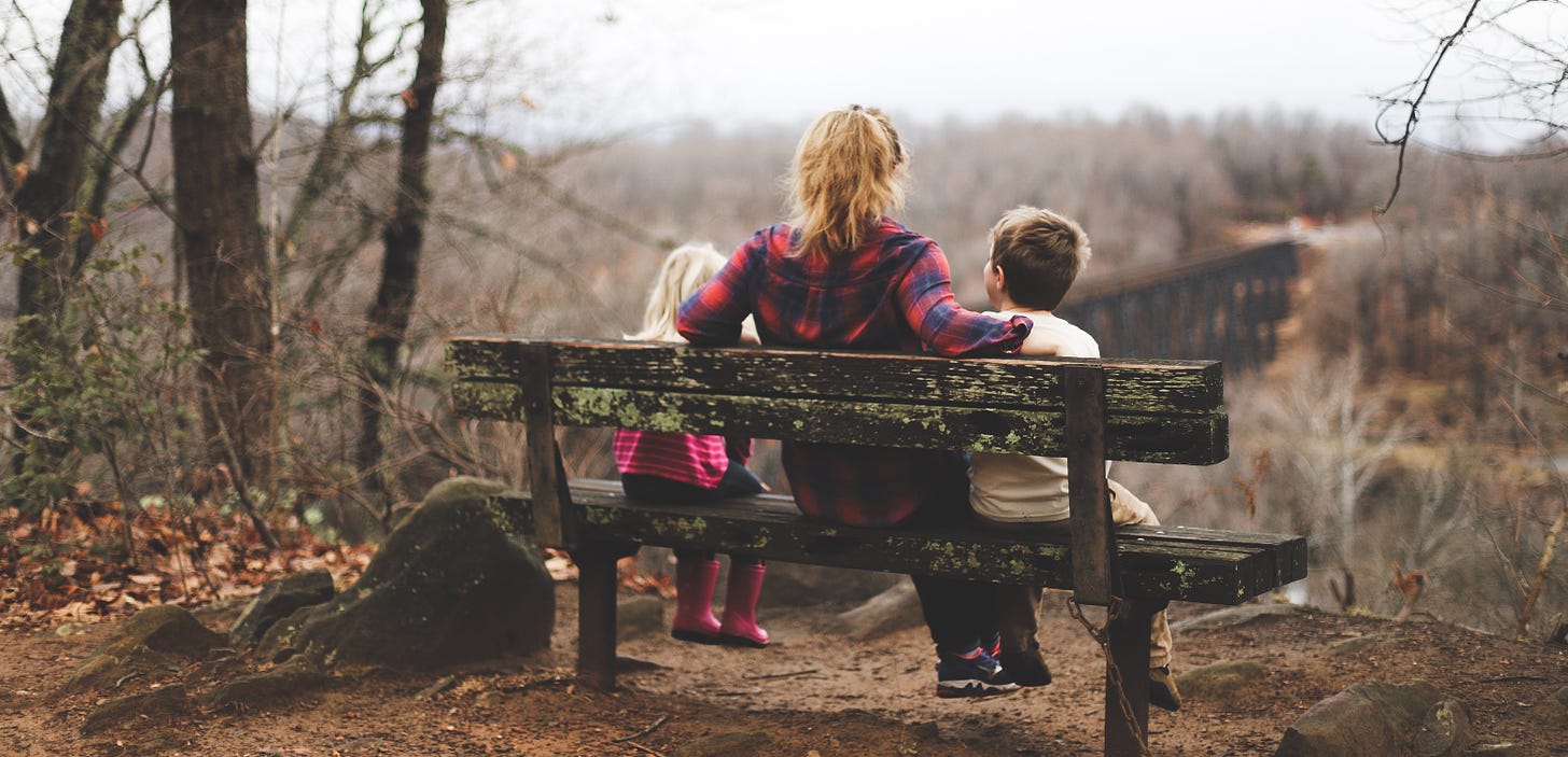 Woman in flannel shirt sitting on bench in the woods with two toddlers on either side of her