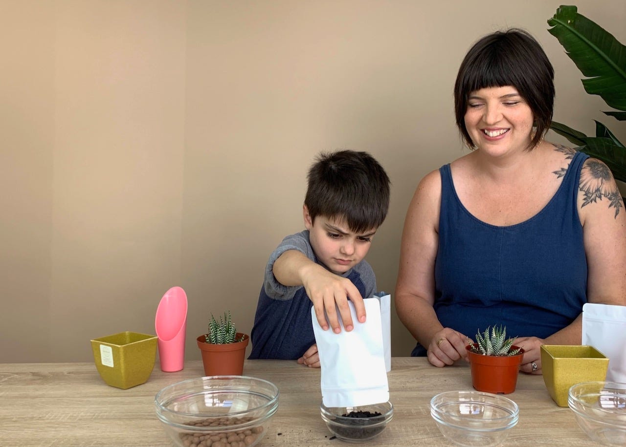 woman smiling next to a kid mixing potting mix into a bowl
