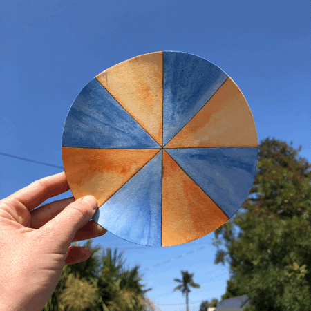 An animated photo loop of a hand holding up a paper circle painted in alternating orange and blue pinwheel slices and spinning it frame by frame.