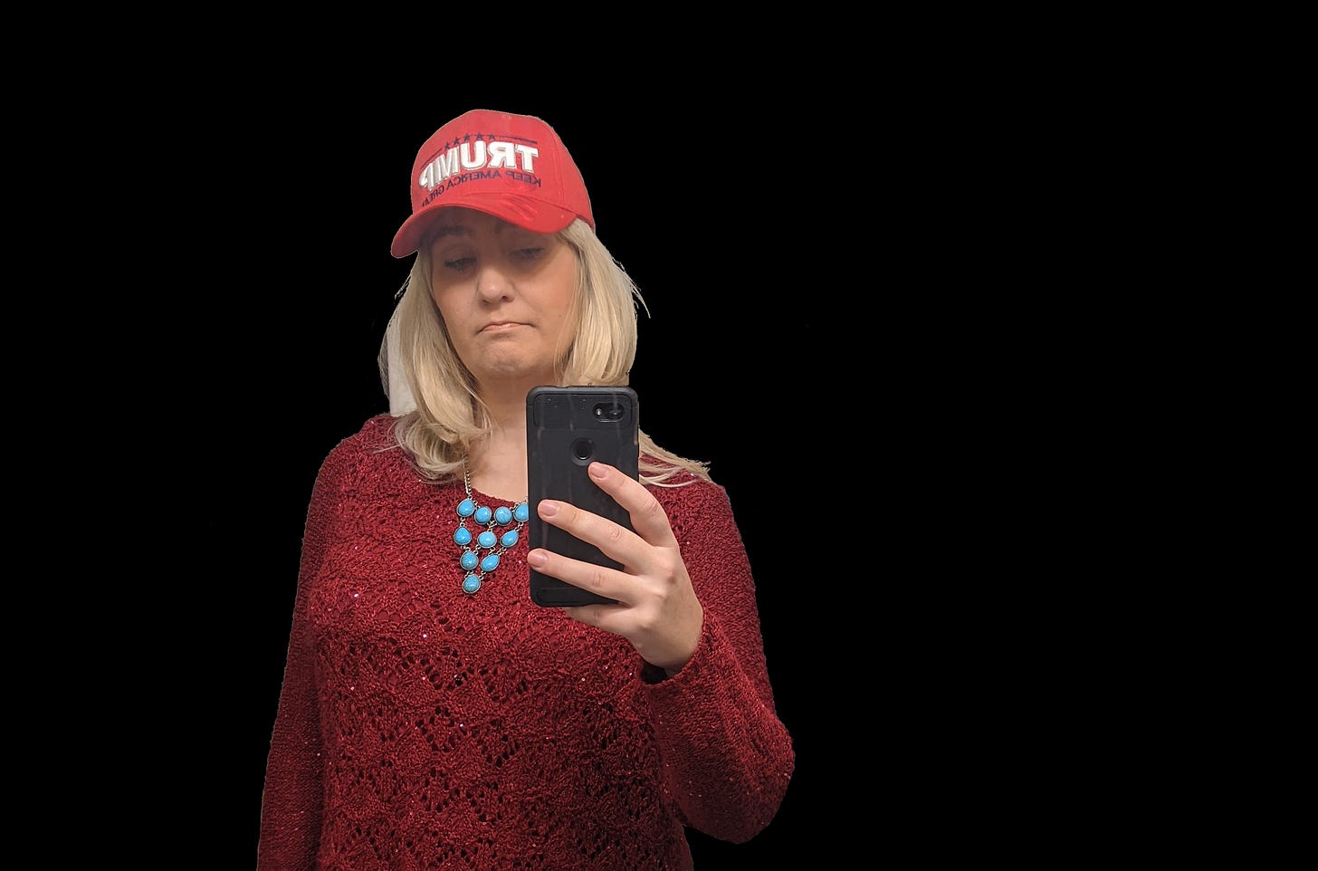 A woman with blonde hair, a red TRUMP baseball cap, and a turquoise necklace looks at her phone. Black background