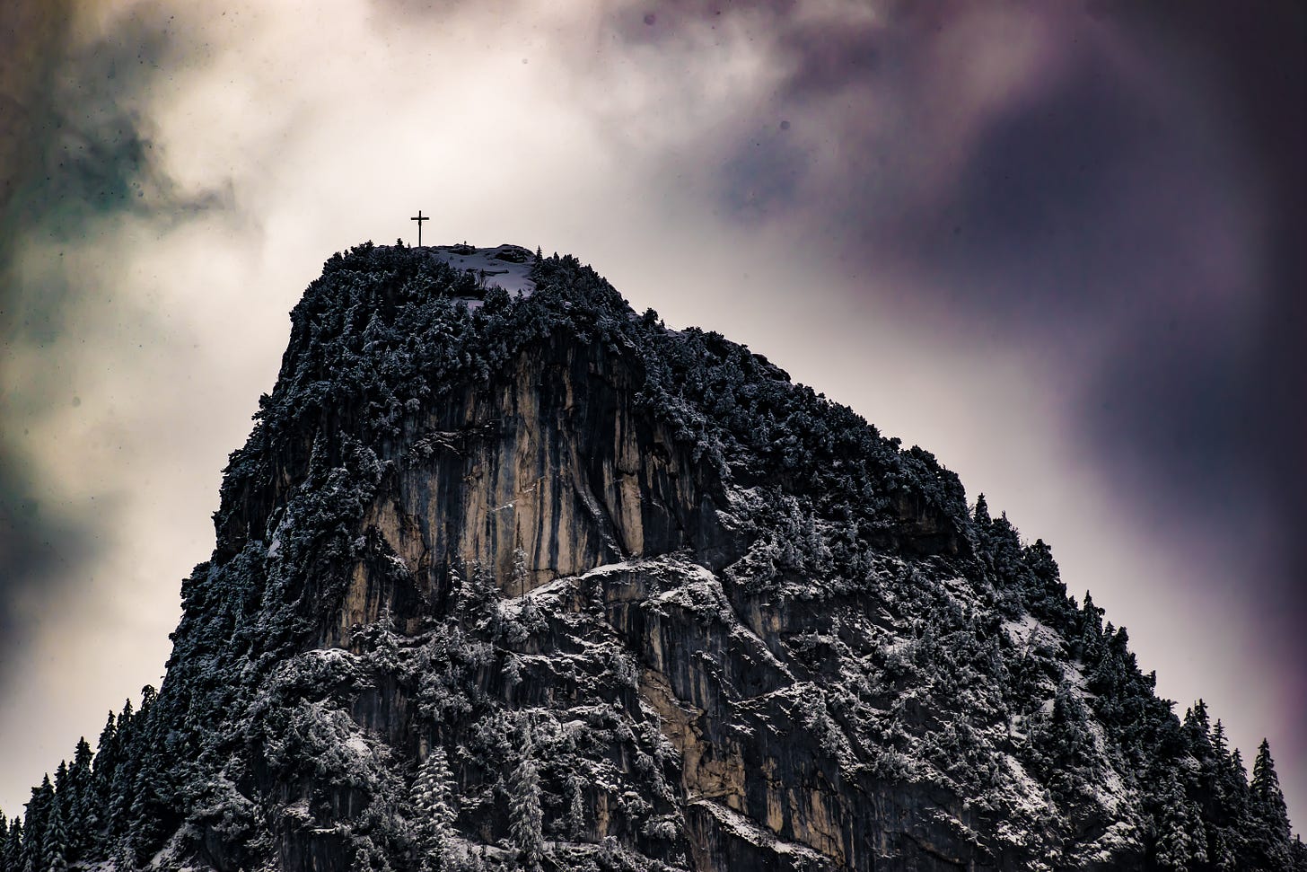 A cross on top of a snow-dusted mountain. 