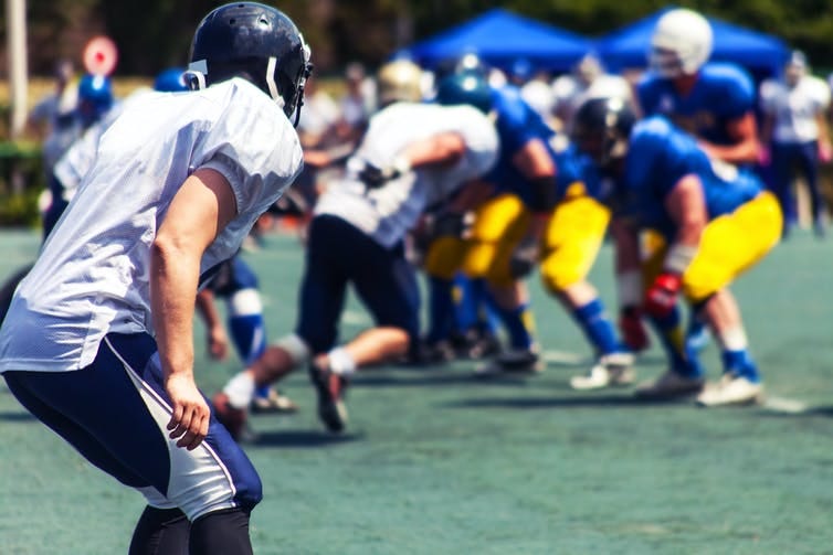 A close up of football players huddled loosely on a field, mid-game