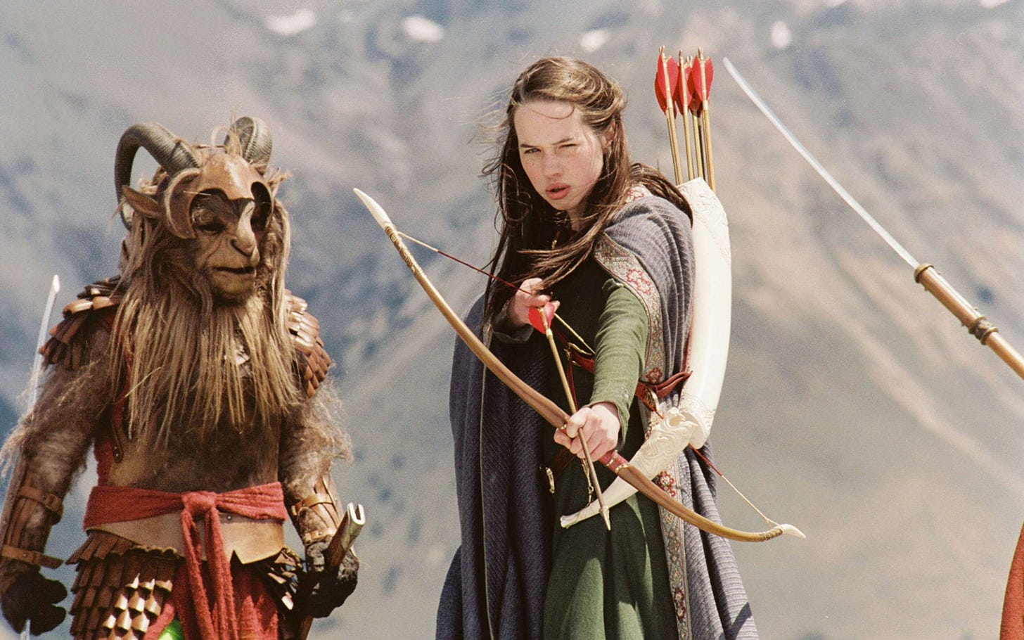 Two figures stand facing the viewer with a mountainside in the far background; to the left is a sort of ram creature with a helmet and other armour; in the centre is a young woman with long brown hair, a cape, and a quiver of arrows, raising a bow