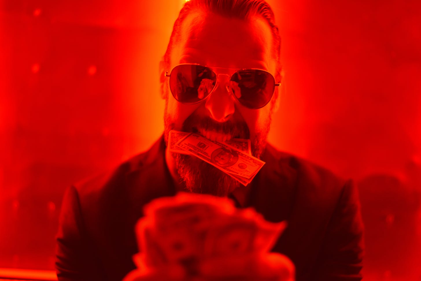 A man wearing dark sunglasses holding money under a red light.