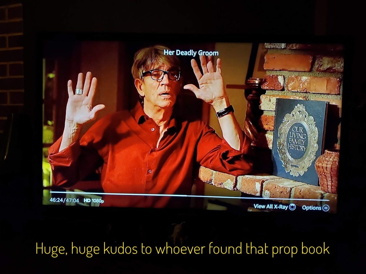 George, holding his hands up next to a book of Our Living Family History, captioned "Huge, huge kudos to whoever found that prop book"