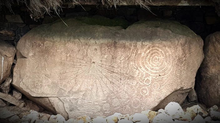 A rectangular stone with broken edges with a beautiful rayed design occupying most of its surface with some small and some larger concentric circular designs.