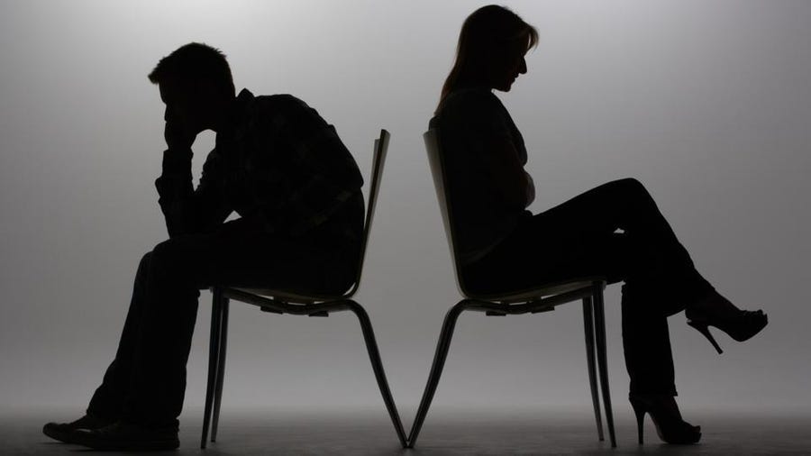 Silhouettes of a man and woman sitting back to back in chairs. He's leaning on his hand she has arms folded.