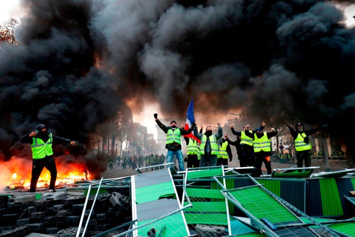 Protestors in high-vis yellow vests shout slogans as material burns behind them and black clouds of smoke billow