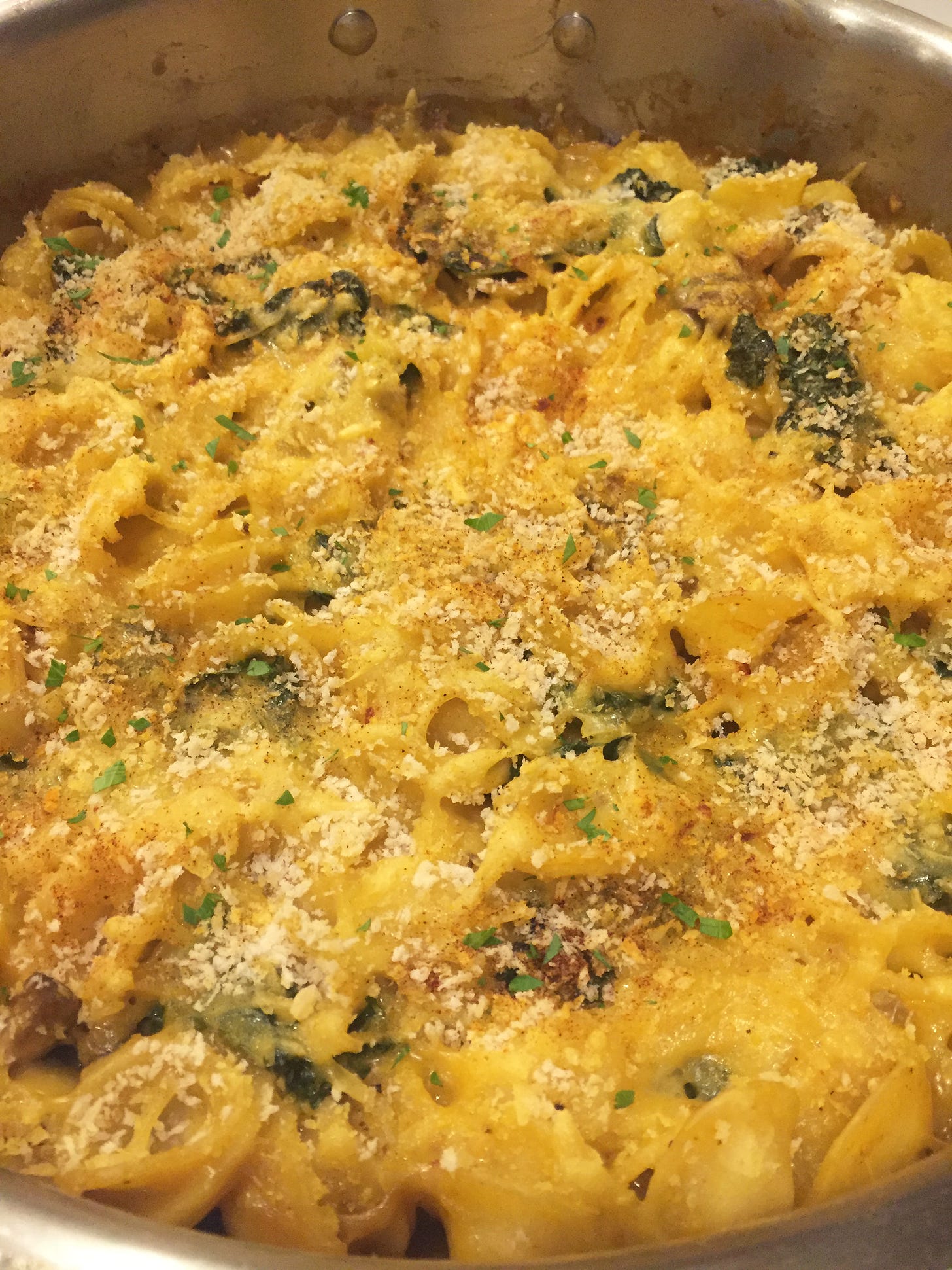 a pan full of creamy, yellow-orange baked mac & cheeze. The top is lightly covered with panko crumbs and paprika, and pieces of kale are visible throughout.