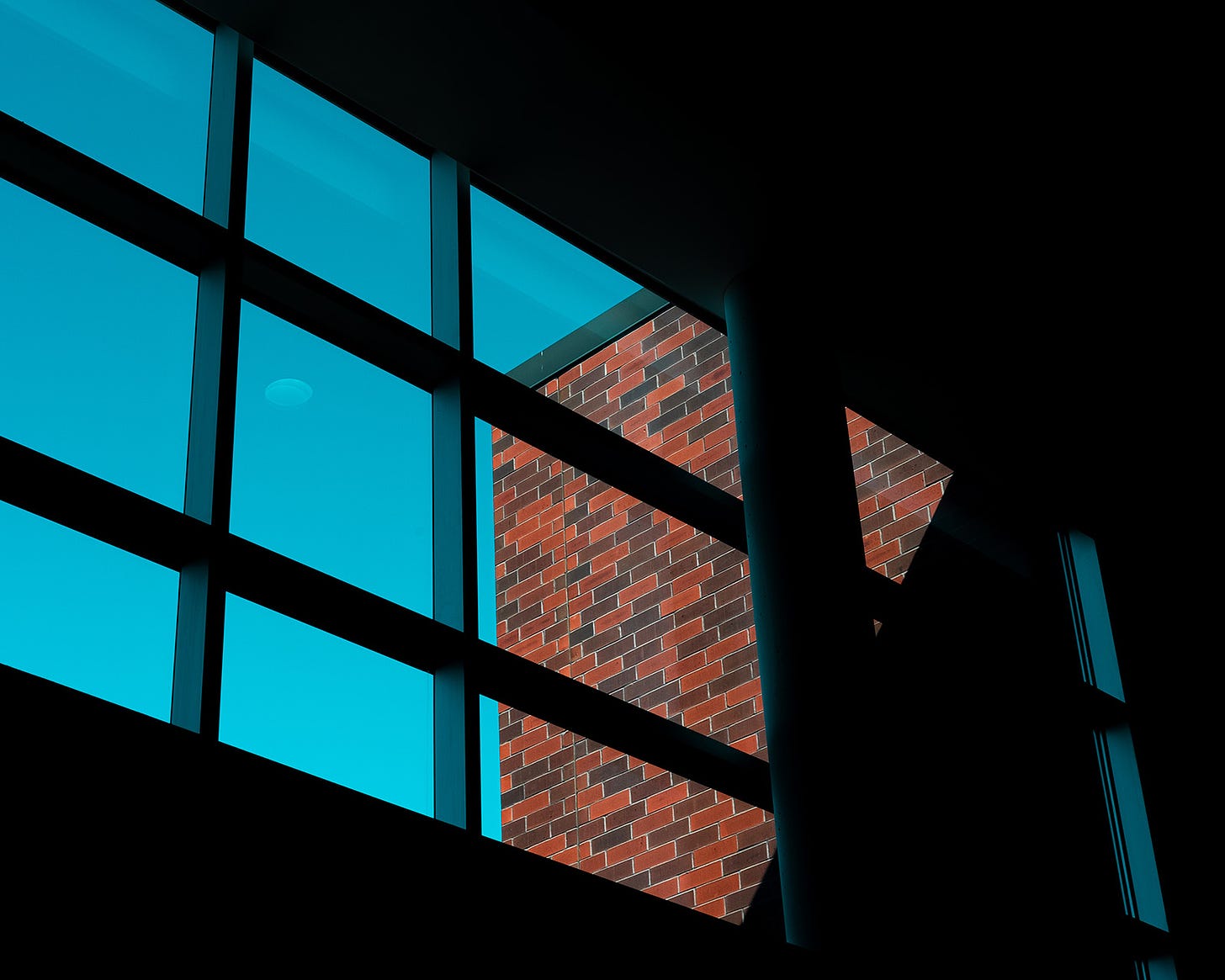 The facade of an orange brick building is viewed through a large window.  A clear blue sky frames the brick building
