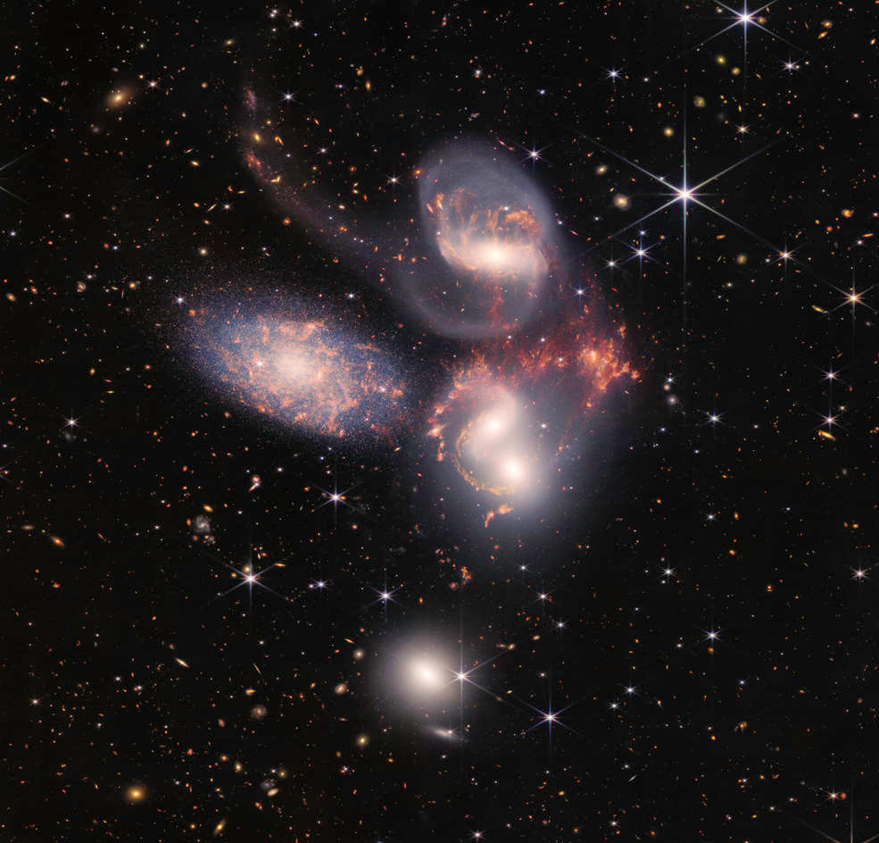 the galaxies in Stephan's Quintet appear as purple-pink swirls against the blackness of space in this JWST image; some foreground stars appear with diffraction spikes from the telescope's mirrors; numerous other galaxies and stars bespangle the image