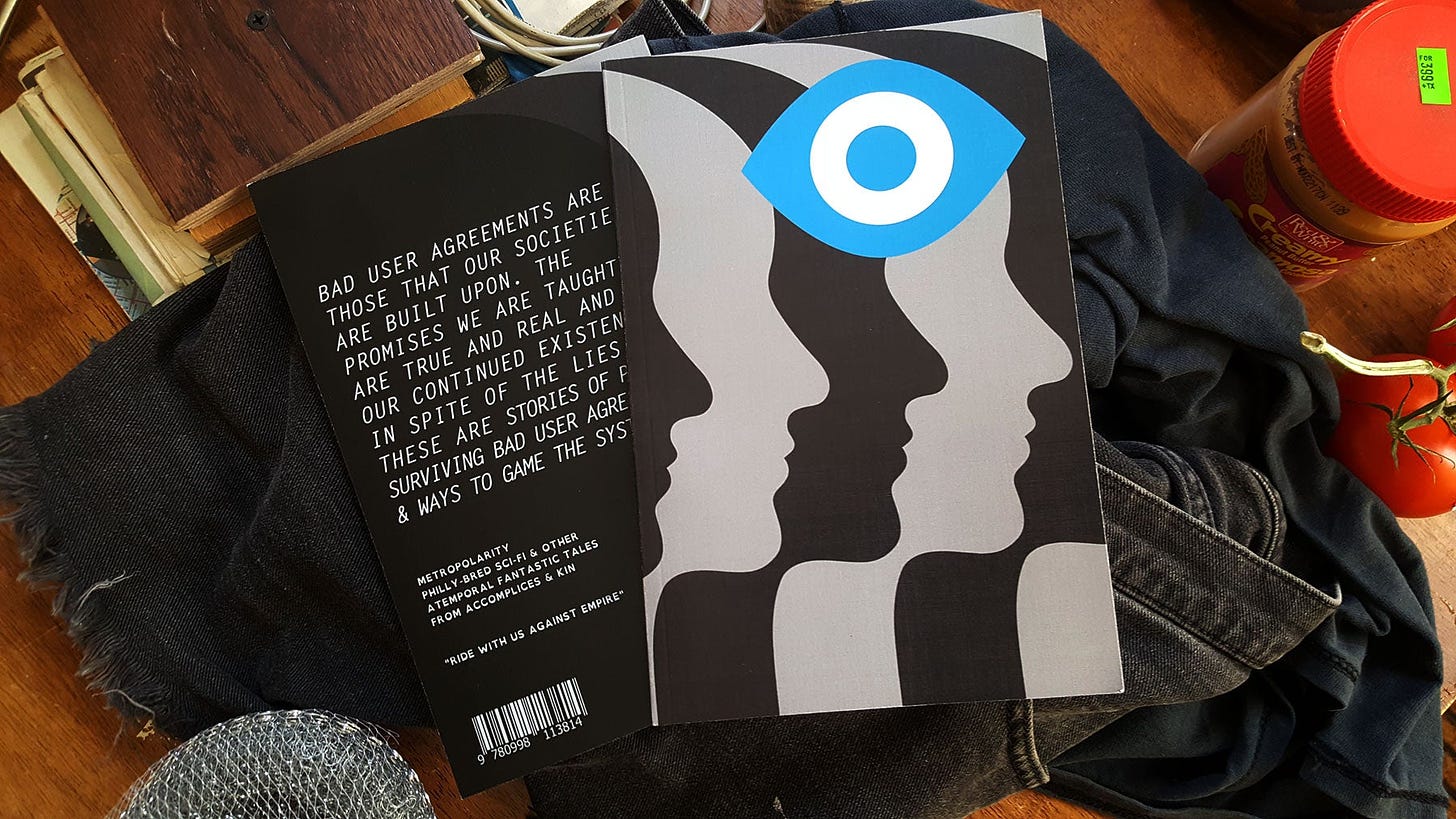 The front and back cover of the book sit on top of a pile of crumpled black laundry, on a table surrounded by random kitchen objects and groceries.