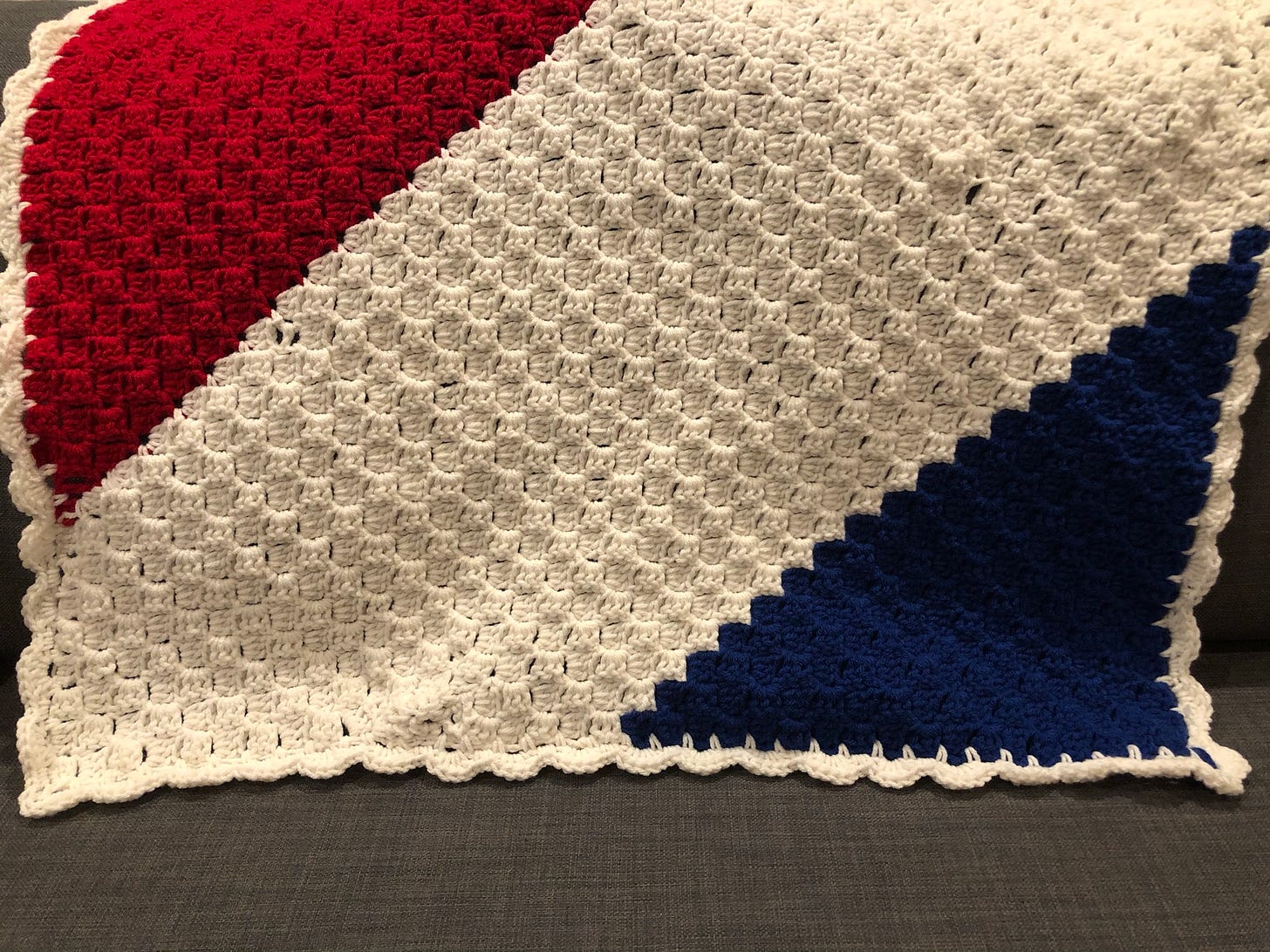 Diagonal red white and blue striped crocheted baby blanket laying over the back of a couch