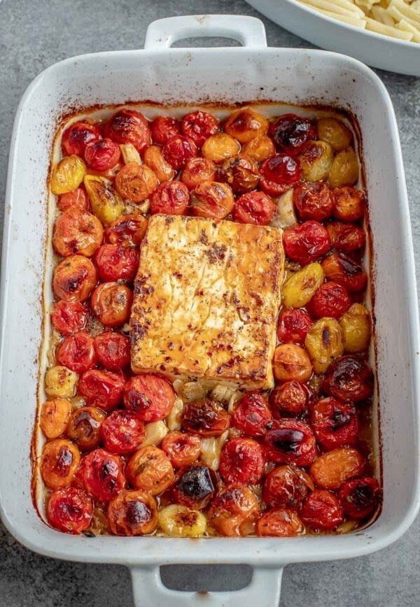 A baking dish with the roasted tomato pasta base cooking together with a block of feta cheese.