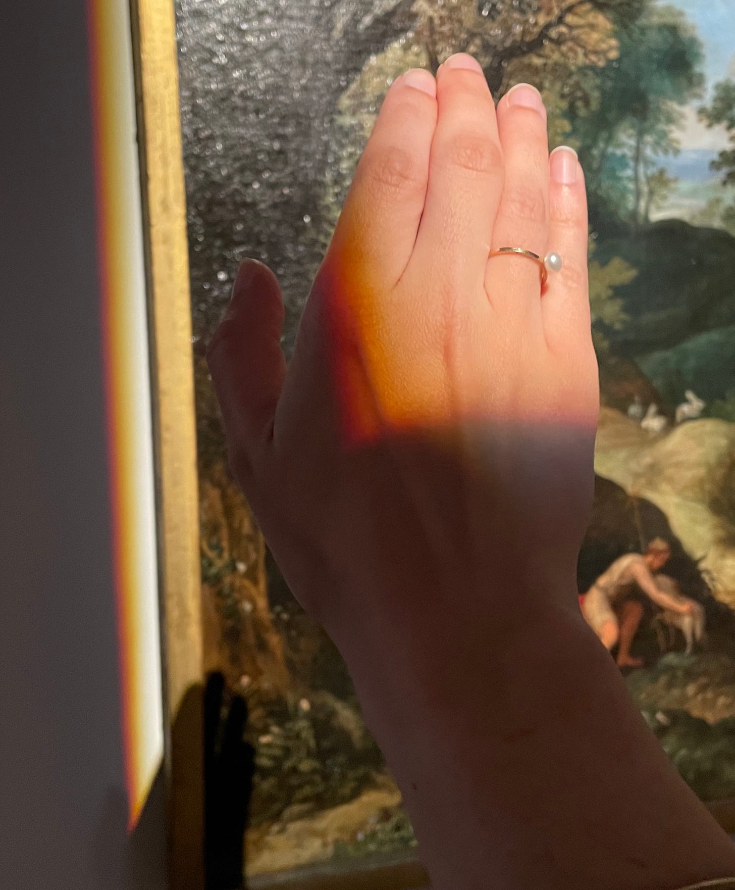 A hand catching the light that is aimed at a painting behind, creating a shadow on the painting
