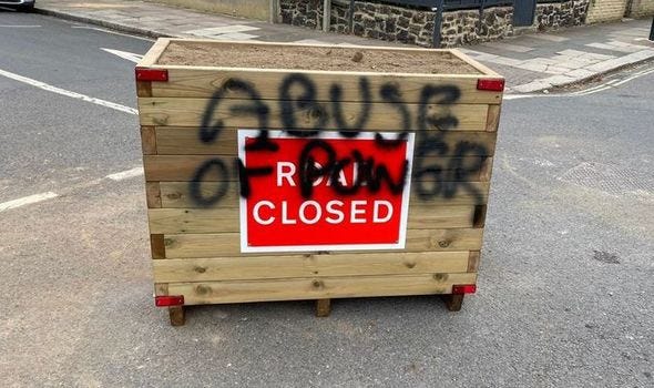 A road closed sign on a planter with grafitti saying "Abuse of power"